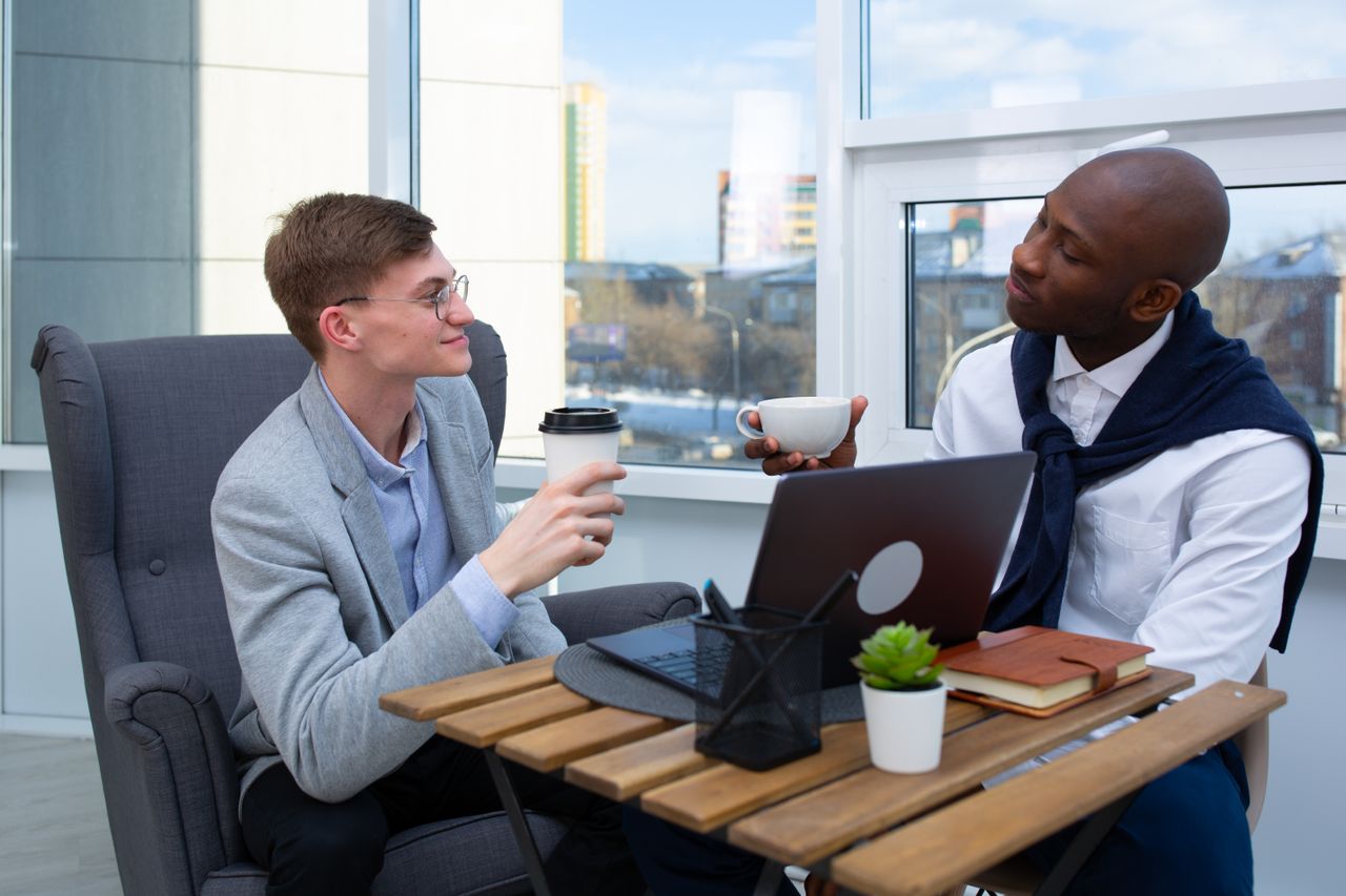 Two businessmen having a coffee meeting in a sunny office with laptops and notebooks.