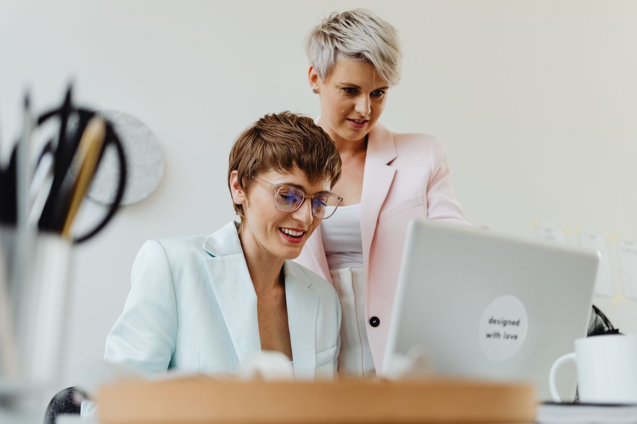 About Two professional women working together happily on a laptop in a bright office setting.